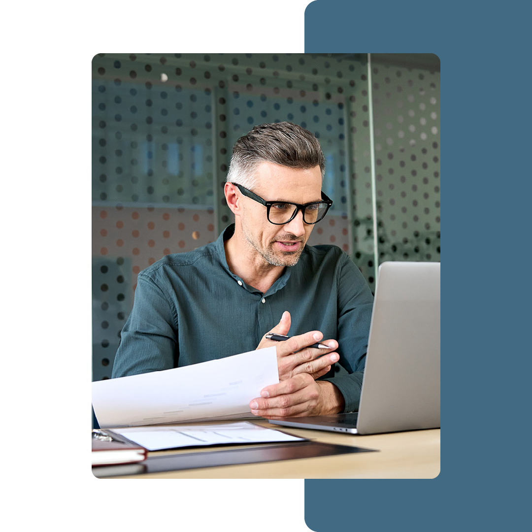 Image of a business professional working on a laptop with pieces of paper in their hand