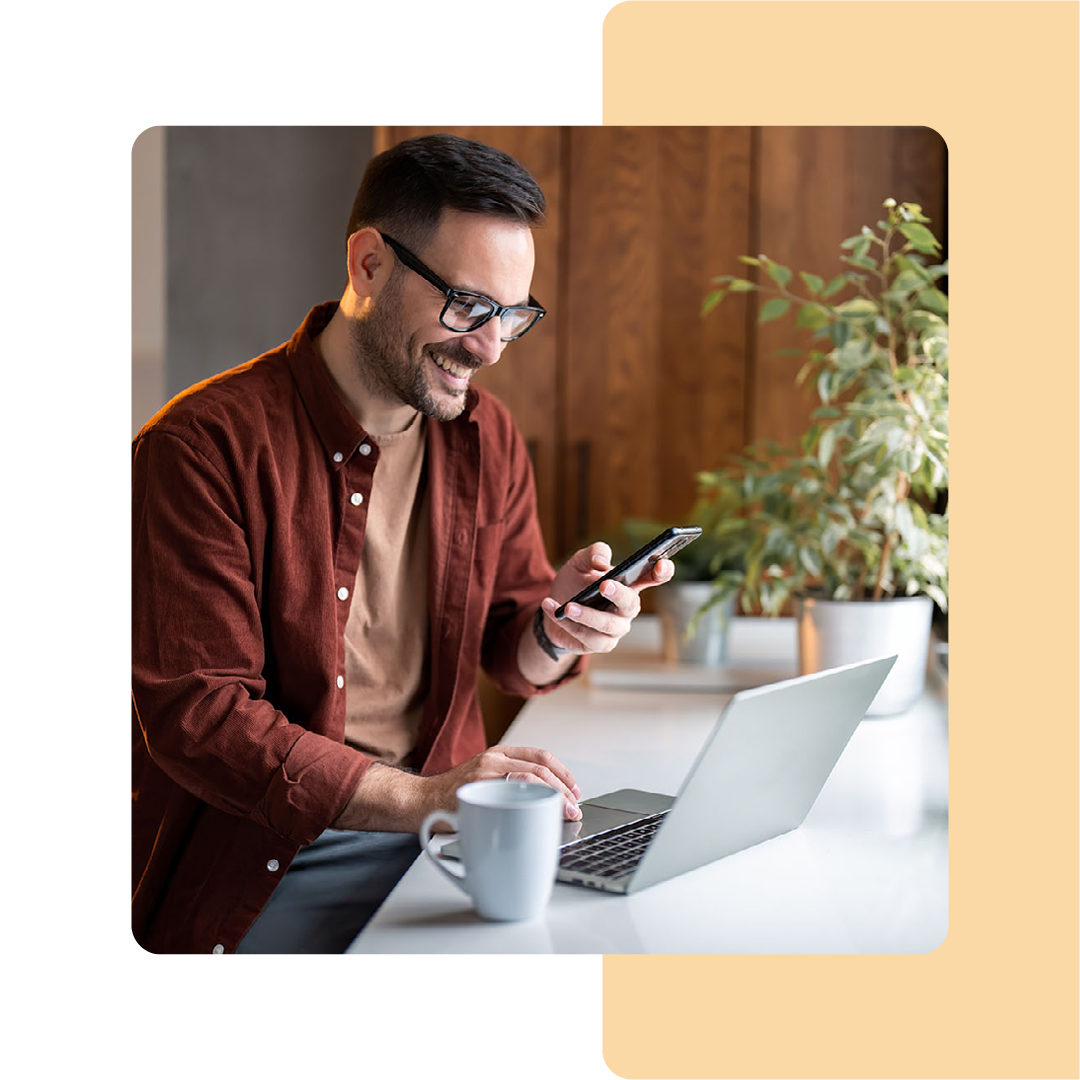 Image of a person working on a laptop and holding a mobile phone