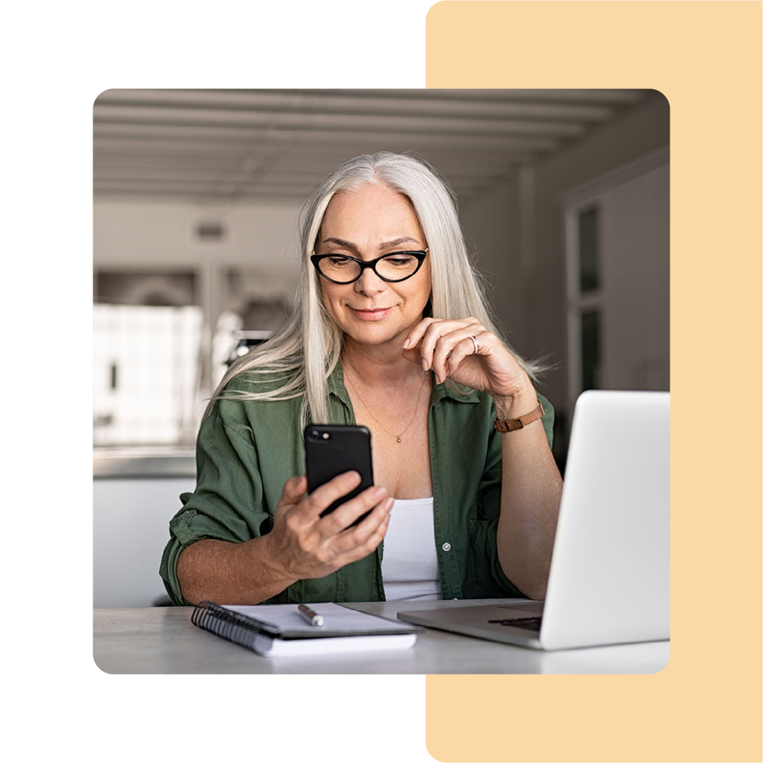 Image of a person holding a mobile phone while working on a laptop