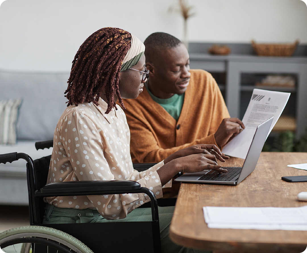 Image of a person in a wheelchair sat working on a laptop with another person