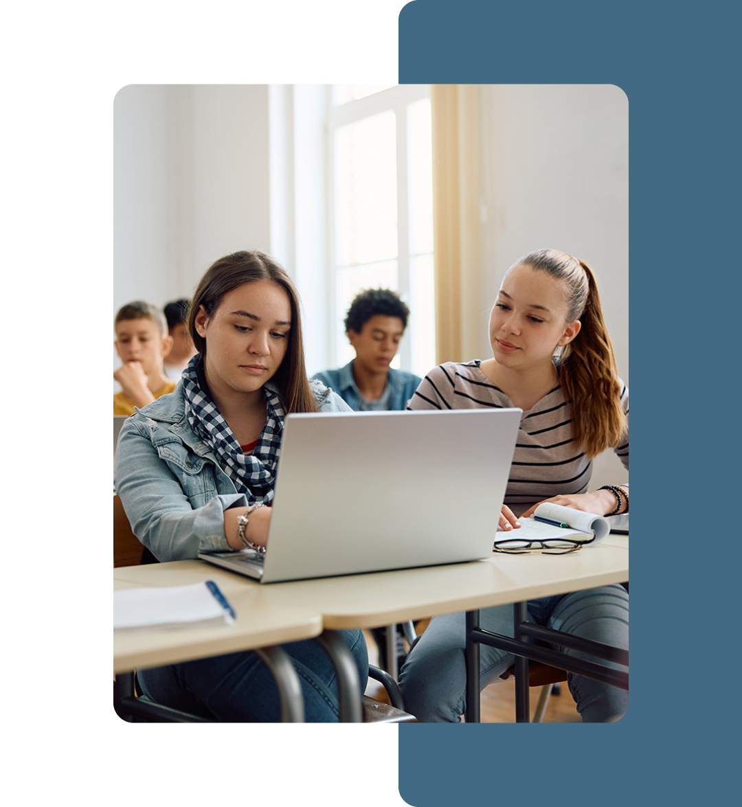 Image of two students sat in a classroom working on a laptop