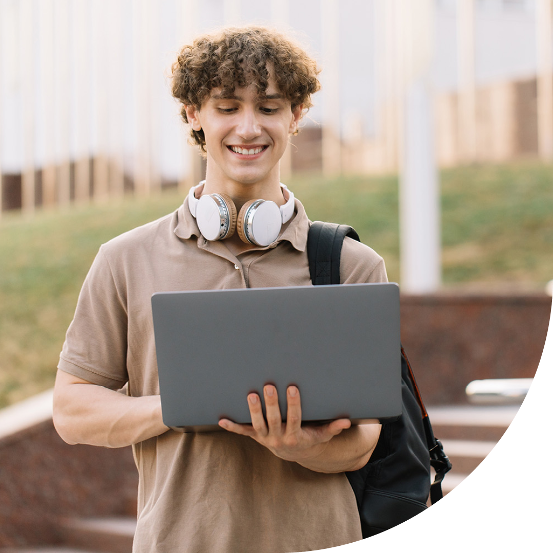 Image of a smiling university student stood on campus holding a laptop