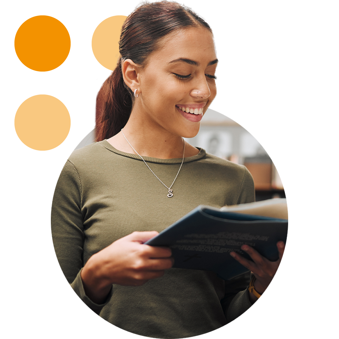 Image of a smiling university student stood in a library reading a book