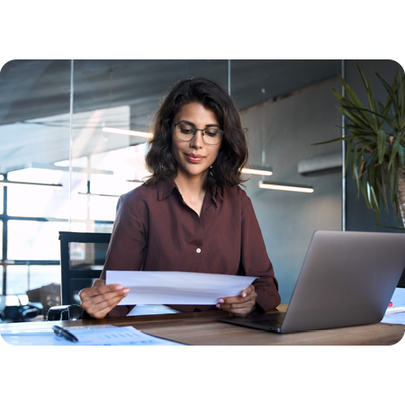 person concentrating on work papers with laptop in front